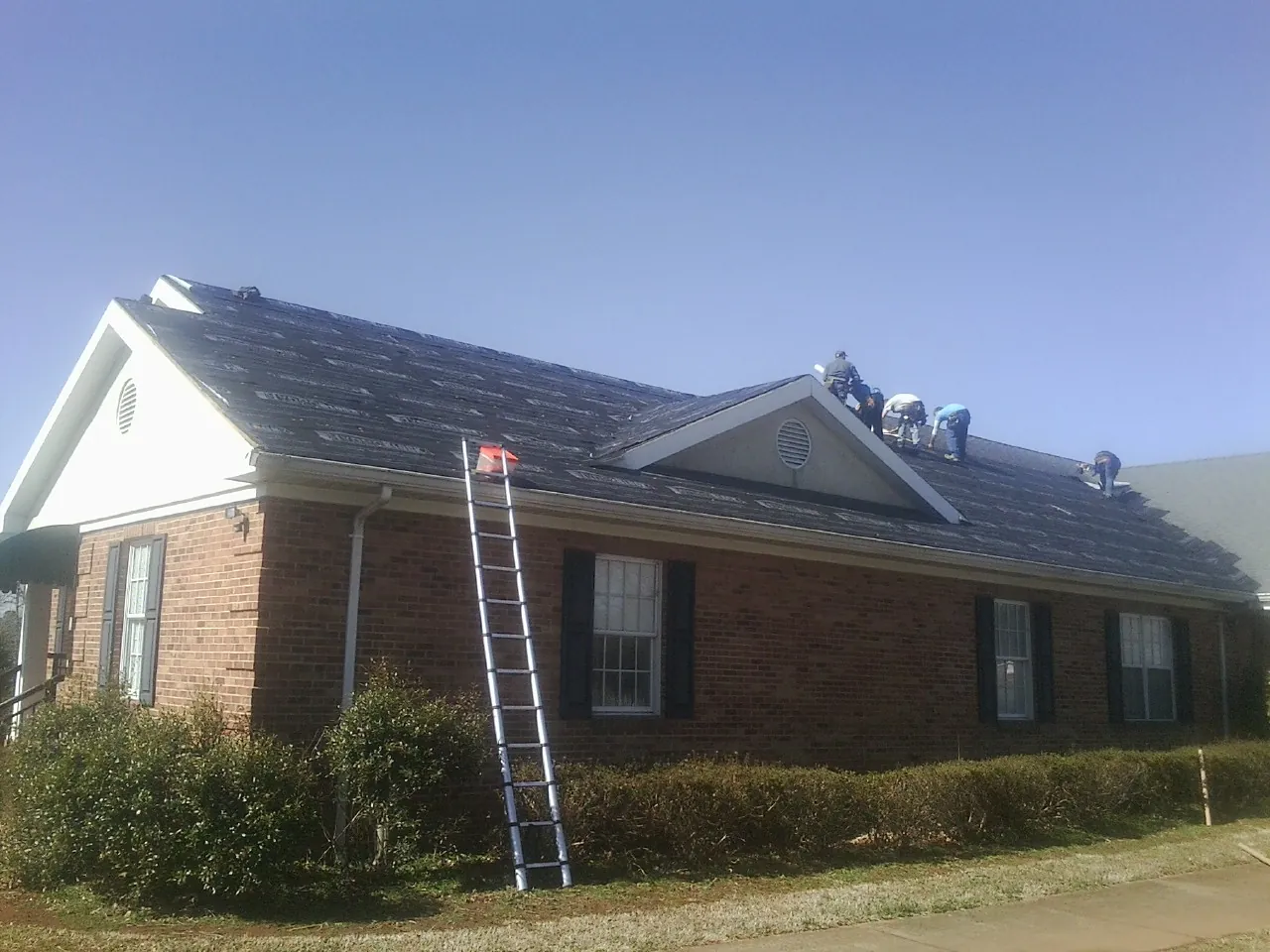 Crew tearing shingles off a brick ranch roof with a ladder set — Metal Roof Repair work by our crew in Cranberry Township