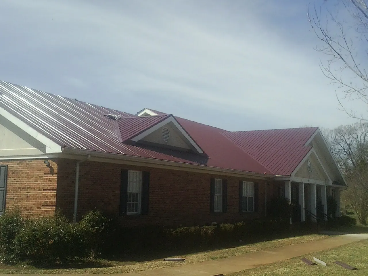 Red metal roof with gabled entries on a long brick building, from a Hail Damage Roof Repair job in Cranberry Township