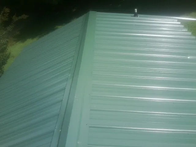 New green metal panels meeting at the ridge of a roof — Flat Roof Repair work by our crew in Cranberry Township
