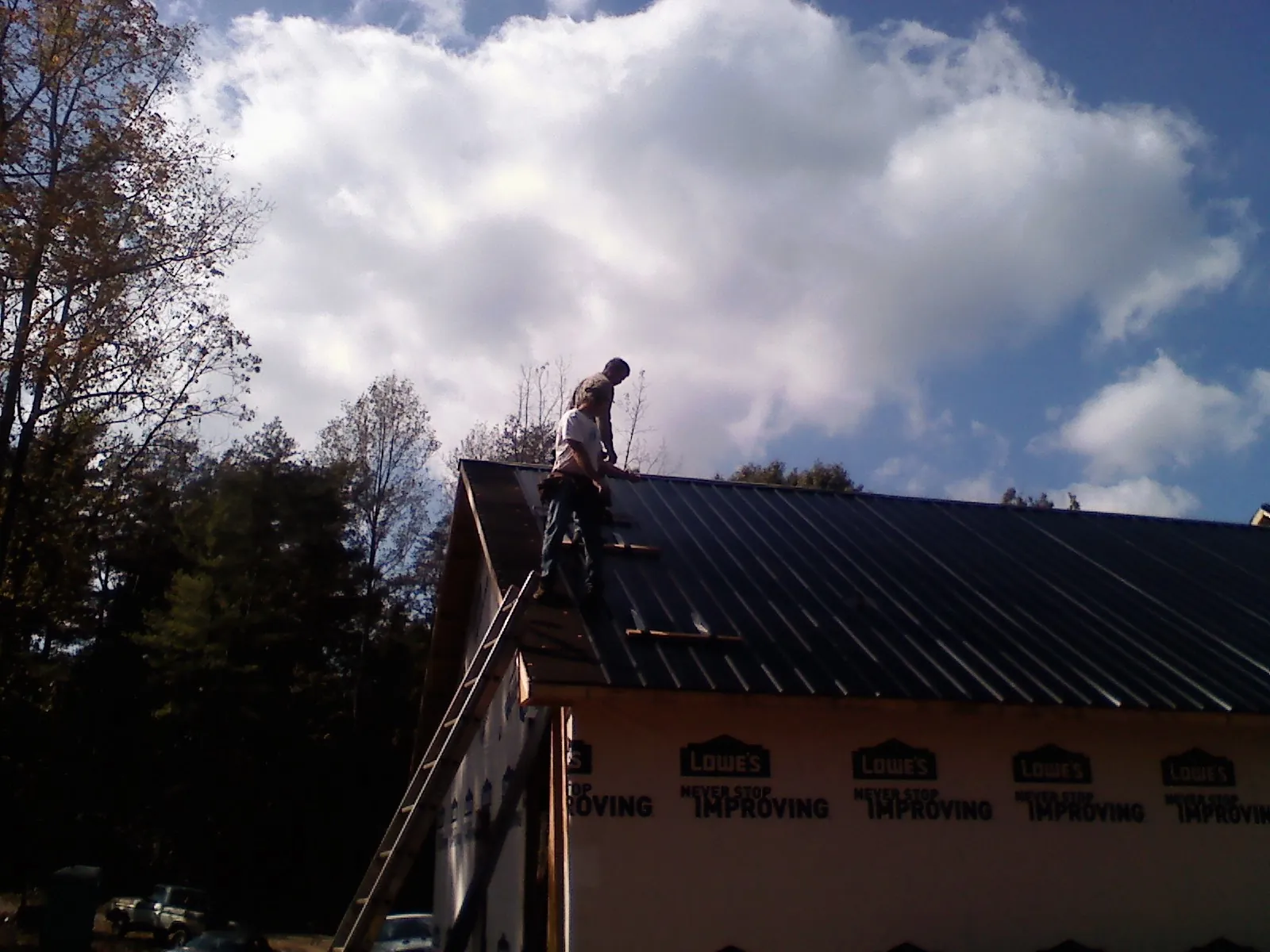 Roofer fastening dark metal panels high against a cloudy sky, from a Roof Inspection job in Cranberry Township