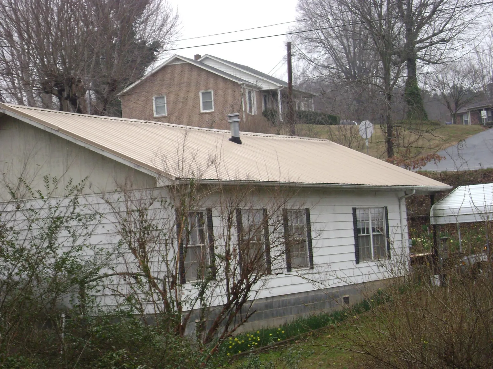 Tan metal roof on a white sided house set into a hillside — Commercial Roofing by Roofing Brothers in Cranberry Township